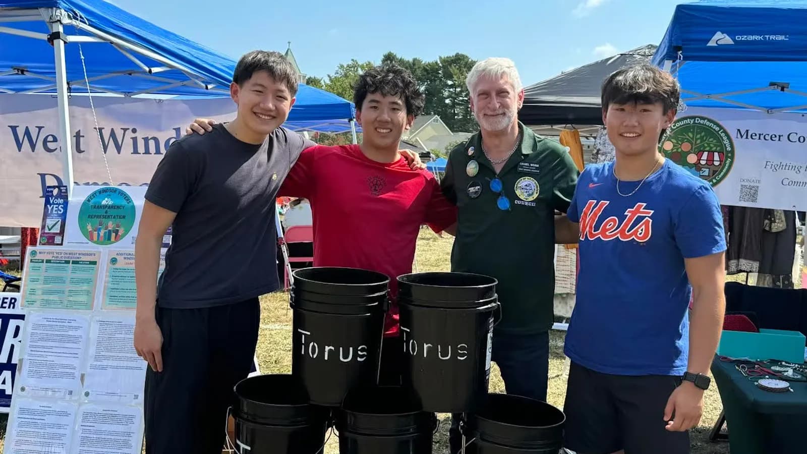 Zikang Jiang, Anthony Woo, West Windsor Councilman Dan Weiss, and David Chen standing behind Torus compost buckets at West Windsor Community Day.