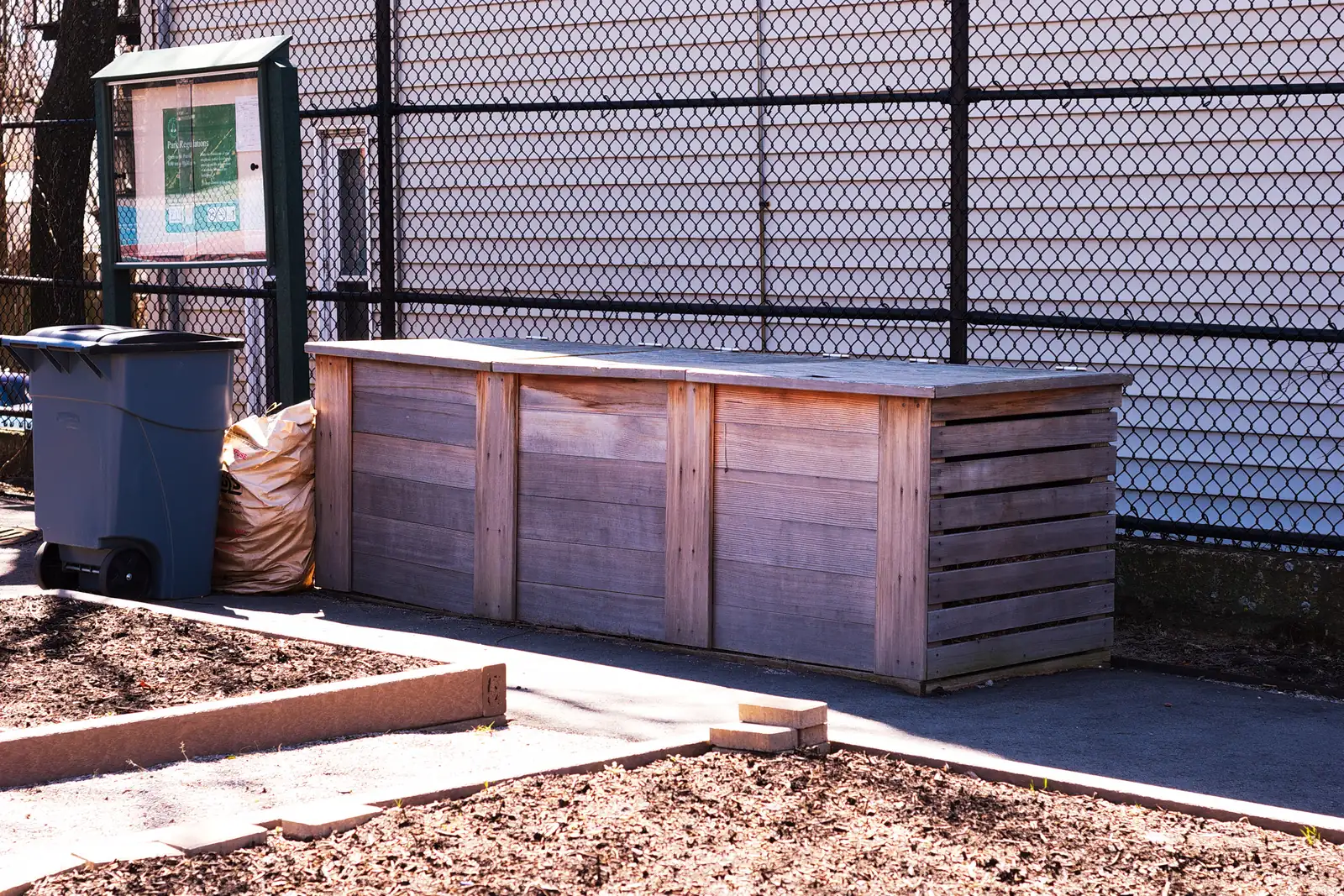 Wooden compost bins in a fenced urban community garden.