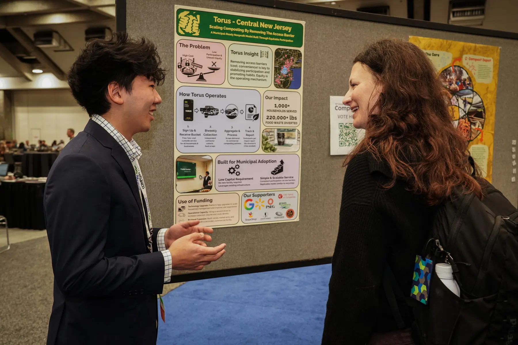 Anthony Woo presenting Torus to a community member beside a composting poster display