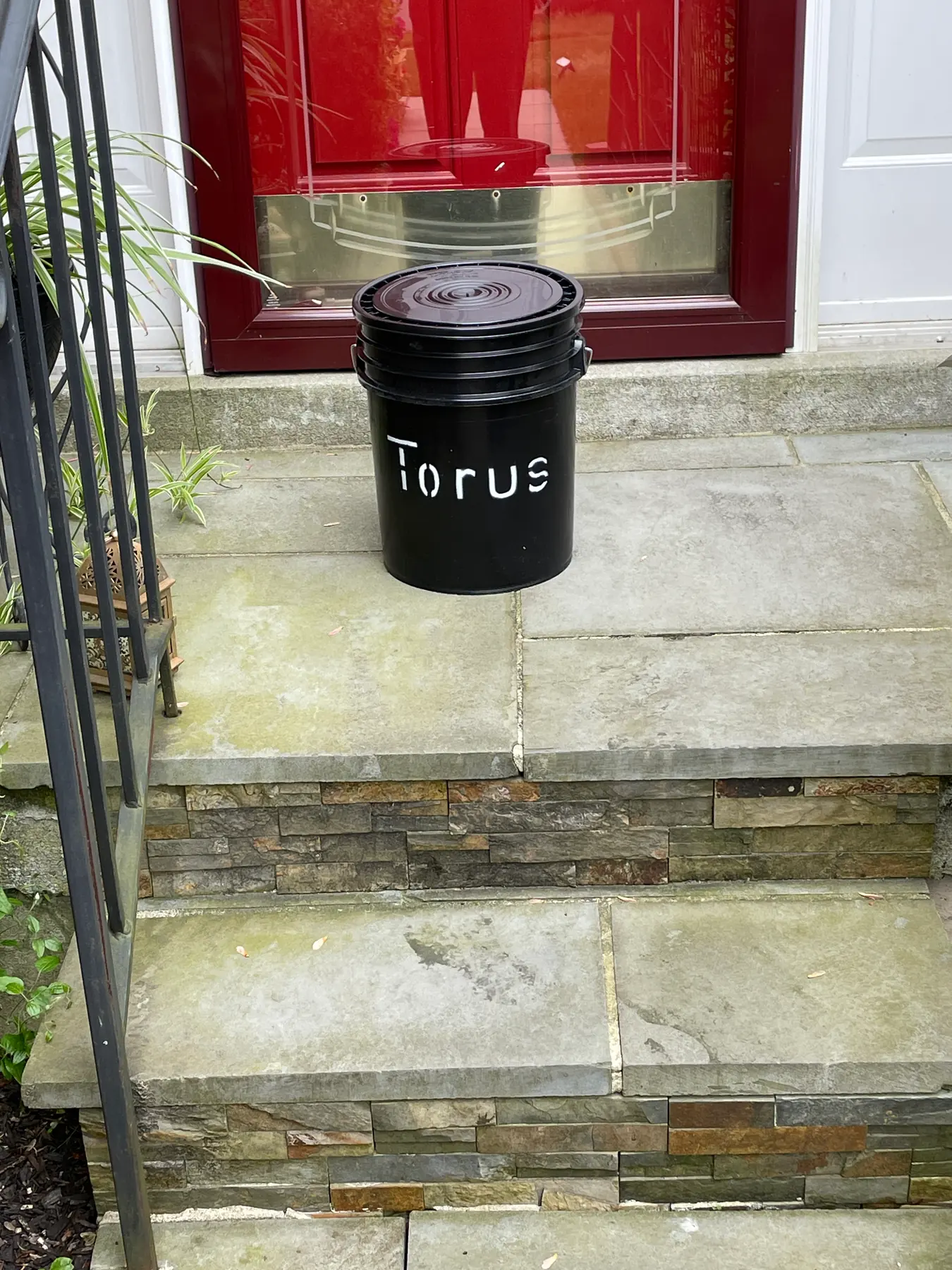 Torus compost bucket resting on a front stoop in a simple residential pickup setup