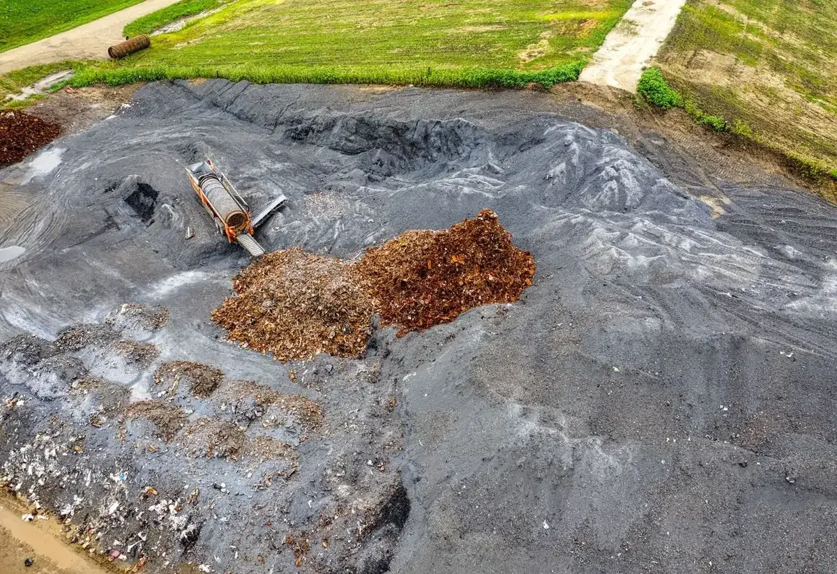 Aerial view of large compost piles and processing equipment at a commercial composting facility.