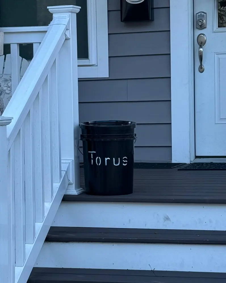 A compact Torus compost bucket on the front porch of a home, showing a space-saving pickup option.