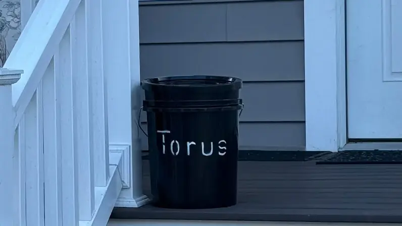 A compact Torus compost bucket on the front porch of a home, showing a space-saving pickup option.