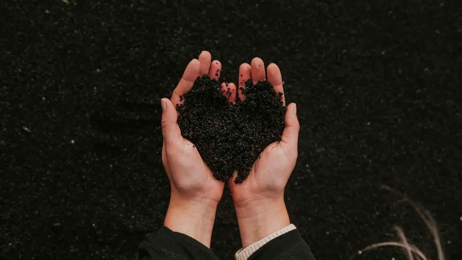 Hands holding dark finished compost above healthy soil, illustrating stable organic matter.