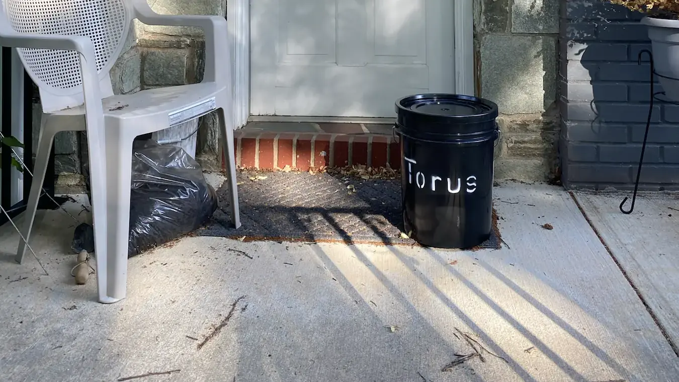 A Torus compost bucket sitting on a residential front doorstep, ready for pickup.